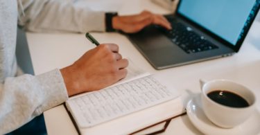 freelancer browsing laptop and taking notes in notebook during work