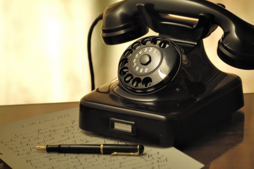 black rotary telephone beside ball pen on white printed paper Dial