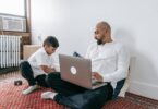 father using laptop and his son playing on the floor