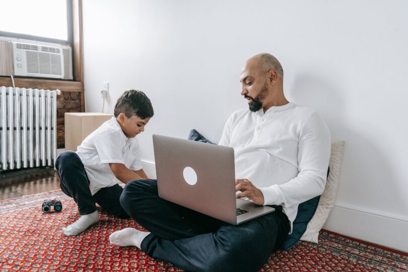 father using laptop and his son playing on the floor