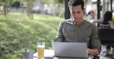 focused black male freelancer using laptop in street cafe