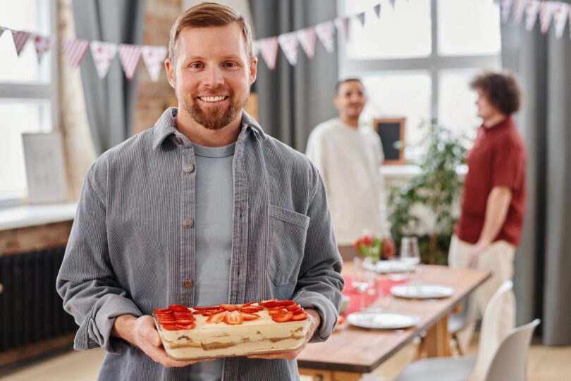 a man in gray long sleeves holding strawberry shortcake while smiling at the camera