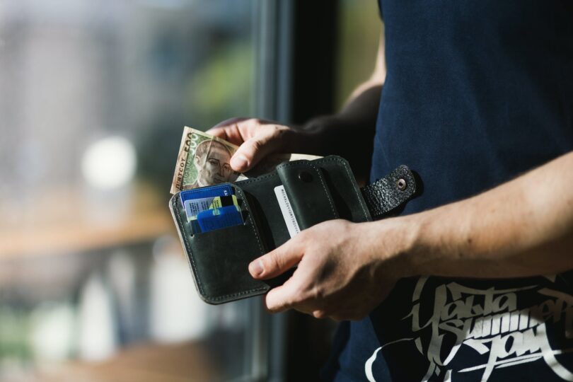 photograph of person holding black leather wallet with money