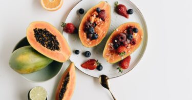 close up photo of sliced papaya with berries on top