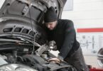man in black jacket and black knit cap inspecting car engine