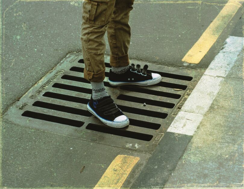 crop faceless man standing on road sewer grating