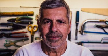 portrait photo of man in white crew neck t shirt with assorted hand tools in background