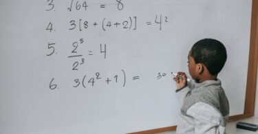 black schoolboy solving math examples on whiteboard in classroom