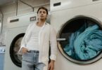 a low angle shot of a man in white long sleeves leaning on a washing machine