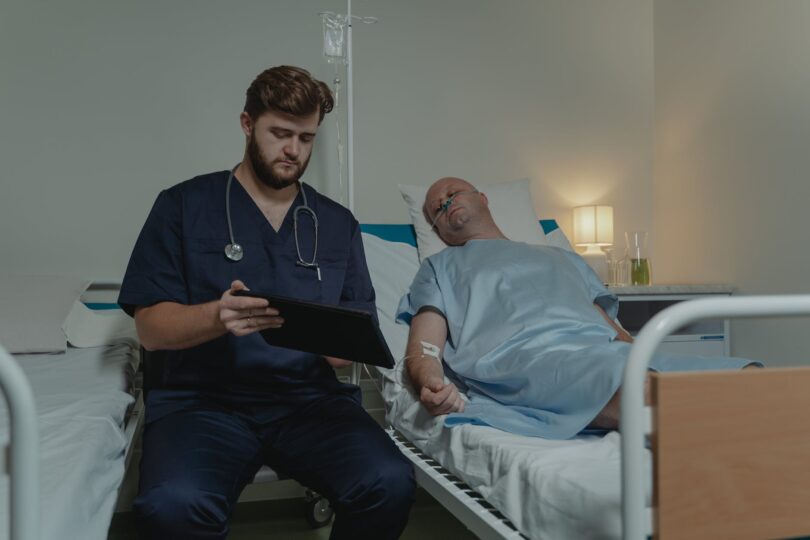 doctor sitting beside a man lying on the hospital bed