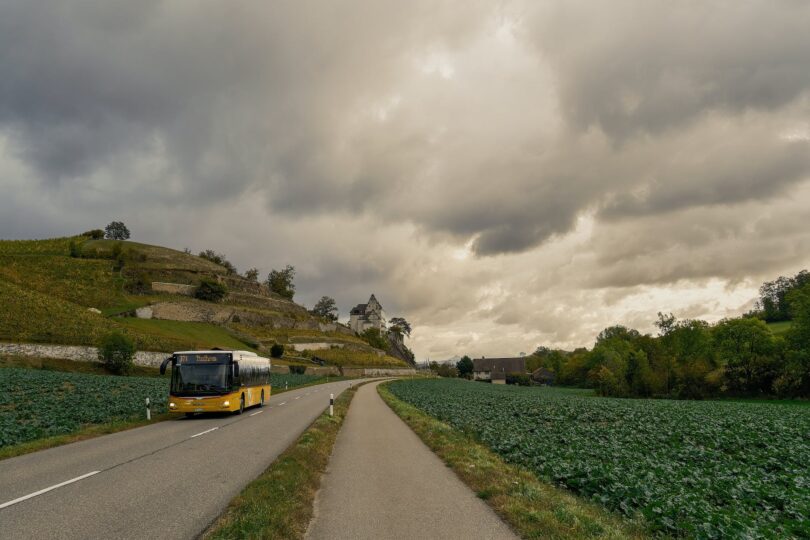 a bus on an asphalt road between fields