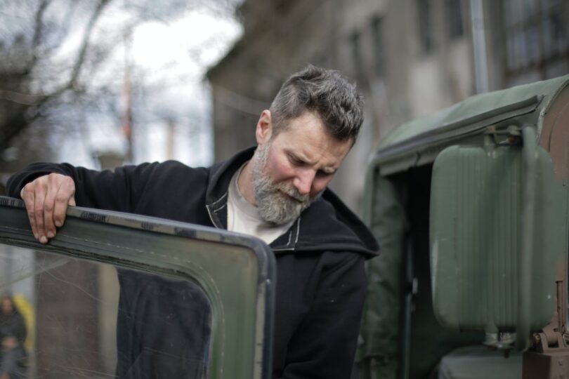 adult bearded mechanic fixing door of car near garage building