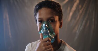 a boy in white shirt holding green oxygen mask