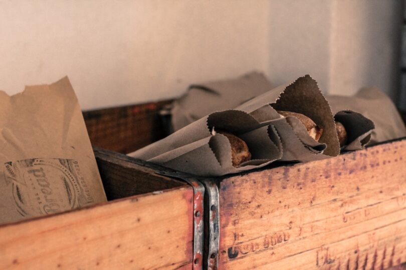 photograph of food packaged in grey kraft paper bags placed in brown wooden open boxes