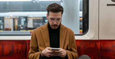 man in brown coat sitting on red seat while texting
