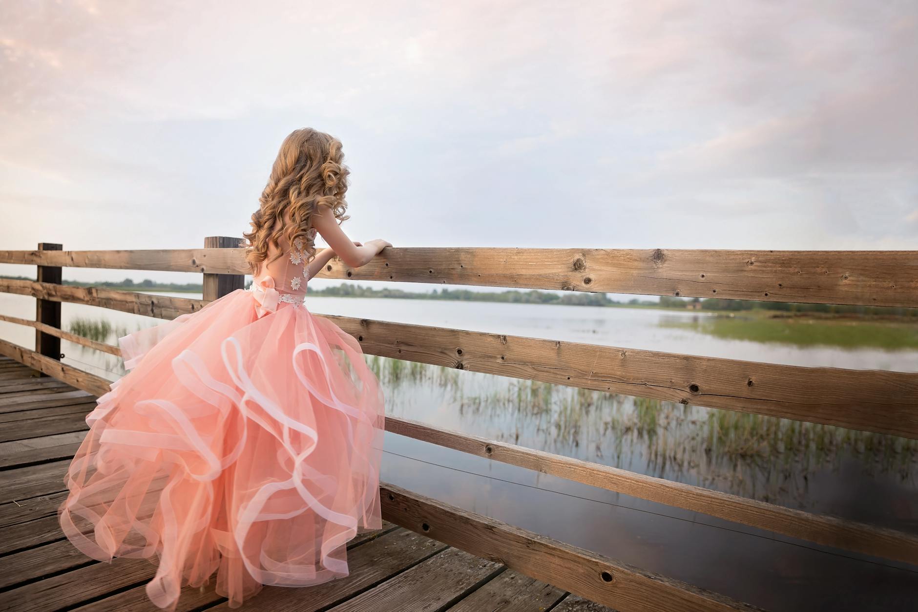 girl in pink gown standing on wooden dock